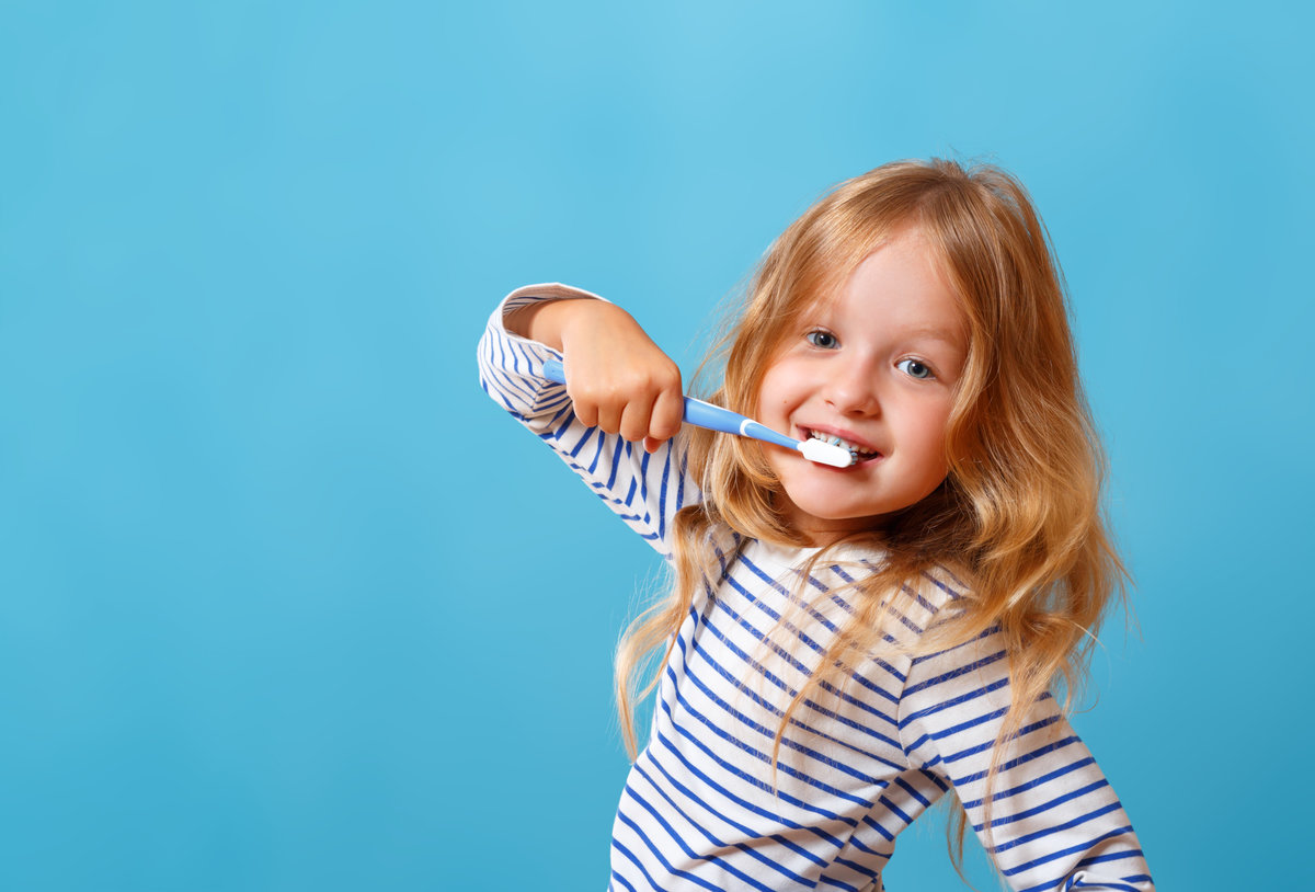A little girl in striped pajamas is brushing her teeth with a toothbrush. The concept of daily hygiene. Isolated on a blue background
